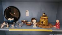 Shelf display with multiple items including bowls, plates, pitchers, and varied animal and child figurines