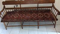 Red runner rug with geometric and floral patterns in blue and white on a wooden bench, showing overall wear.