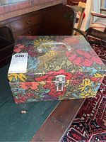 Closed floral patterned sewing box on a wooden table with metal latch and clear handle