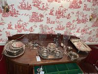 Wide view of the table showing most of the silver plate items including trays, tea service, bowls, flatware, candelabra, and glass hurricane globes