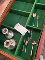 Photo showing two sterling candlesticks, two small fork and spoon sets, small ladle, and spice scoop in a green felt-lined tray.