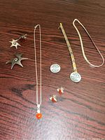 Full view of sterling silver necklace with carnelian pendant, geometric earrings and pin, patterned chain, and smooth chain on wooden backdrop.