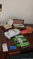 Photo showing white vintage toy car, red double-decker bus, multiple decks of playing cards in boxes, and a bridge playing manual on a wooden table.