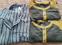 Photo of two folded yellow and grey pajama tops with buttons and one blue striped button-up shirt.