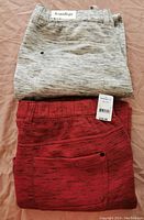 Two folded pairs of jogger pants: one light grey marled and one red with price tag shown
