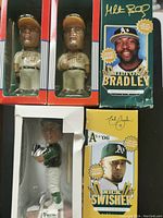 Two Milton Bradley bobbleheads unopened in original red and white packaging, one Nick Swisher bobblehead in original yellow and white box, all Oakland Athletics themed showing player images and signatures.