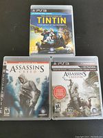 Front view of three PS3 game cases: Assassin's Creed, Assassin's Creed III Signature Edition, The Adventures of Tintin: The Secret of the Unicorn