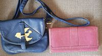 Photo of navy blue leather purse with gold-tone bird decoration beside pink leather wallet showing exterior.