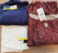 Three women's tops laid out, folded blue and white shirts, and unfolded red floral blouse with tag visible.