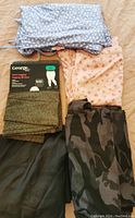 Various women's 4XL bottoms including pajama pants, tights, and camo pants shown folded on bed