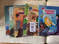 Seven vintage Disney hardcover children's books stacked on a white surface. Covers feature classic Disney characters from various stories including The Aristocats, Pinocchio, Sleeping Beauty, and others.
