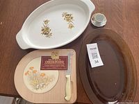 Photo showing all items in the lot: white ceramic serving dish with floral pattern, brown oval glass dish, wooden cheese board with cheese knife, small espresso cup and saucer.