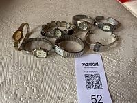 Seven assorted women's watches arranged in two rows showing various metal bands and dial shapes on fabric surface.