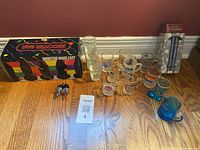 Overview of all items including shot glasses in original box, mugs with logos, blue plastic pourers and measuring cup, and boxed wine pourer set