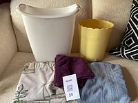 View of all items including two trash cans, folded towels, bath mat, and partially visible shower curtain arranged on a couch