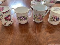 Four bone china coffee mugs with various floral decorations arranged in a row on wood surface.