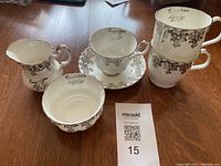 View of all five pieces: cream jug, sugar bowl, cup with saucer, and two coffee cups arranged on wood table