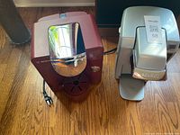 Picture showing front and side view of Bosch Tassimo and Keurig coffee machines side by side on wooden floor, highlighting their design and size.