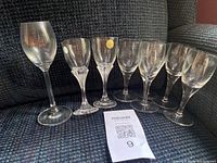 Eight crystal glasses grouped on dark fabric sofa with auction tag in front
