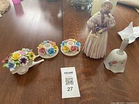 Photo showing four decorative items: a lady figurine, two floral candleholders, a ceramic floral wheelbarrow, and a ceramic handbell.