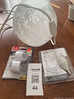 Photo showing frosted glass nightlight lamp shade with white cord, LED replacement bulb in packaging, and white lamp holder adapter in packaging alongside a lot tag