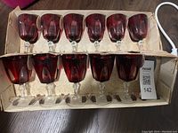 Box holding 11 red glass goblets with clear stems, arranged in two rows inside original packaging.