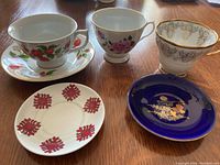 Top-down view of three cups and five saucers arranged on wooden surface, showing detailed floral and decorative patterns on each piece.