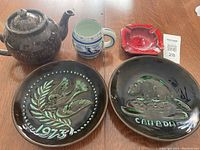 Photo showing the set of brown glazed teapot, blue and white mug, red ashtray, and two brown ceramic plates with relief designs.