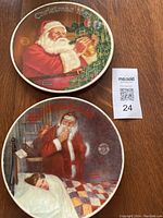 Top side of the two Norman Rockwell Christmas plates showing the festive artwork of Santa Claus for years 1984 and 1985.