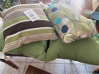 Four outdoor cushions placed on a chair, showing patterns and colors clearly including green, beige stripes and abstract circles in blue and green.