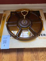 Photo of 13-inch round plastic party server with six divided sections and brass-colored center handle on original box.
