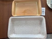 Two rectangular Blue Mountain Pottery bakeware dishes displayed on a wooden surface, one beige with speckled glaze and one solid tan.