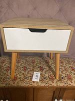 Front view showing the whole table with white drawer and angled wooden legs. Small chip visible on drawer front.