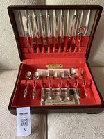 Opened chest showing complete silver flatware set with knives, forks, spoons, and serving utensils arranged in red felt lining.