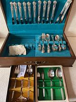 Photo shows the open wooden chest lined with blue velvet containing organized sets of silver flatware including forks, knives, spoons and some serving utensils.