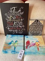 Four canvas artworks of various sizes on a couch showing two inspirational quote canvases and two bird illustrations