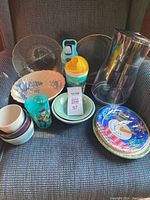 Shows various kitchen items including Brita water pitcher, glass and pottery bowls, kids sippy cups, and holiday paper plates on a dark blue fabric surface.