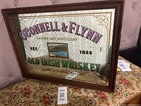 Vintage mirror wall art with O'Connell & Flynn Old Irish Whiskey advertisement framed in wood showing colorful text and a bay scene.