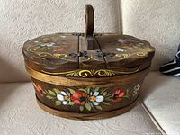 Side view of the vintage wooden sewing box showing floral hand-painted decoration and hinged lid with handle.