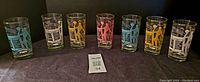 Full set of 7 vintage 1950s highball glasses showing different colors and designs, aligned side by side.