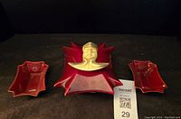 Front view of red ceramic covered box with sculpted Asian bust lid alongside two matching open dishes.