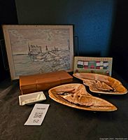 Full lot view showing framed artwork, brown case survival kit, boxed jacket coasters, two MCM ceramic ashtrays, and white ceramic ashtray.