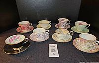Photo showing all eight vintage china teacups and saucers in assorted floral and patterned designs, arranged together on black background