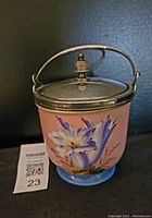 Front view of the antique biscuit jar showing the hand-painted flower design, silver lid and handle, and pink body on blue base.