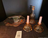 Photo showing the entire set: pink etched glass bowl, liqueur flask with stopper, and two candle holders with white candles on a dark surface