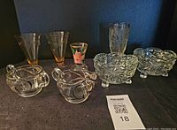 Showcases the entire glassware collection, including two footed pink engraved glasses, clear etched tumblers, footed pressed pattern bowls, cream and sugar containers with silver overlay.