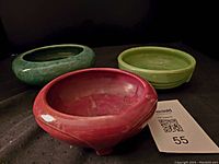 Photo showing set of three shallow pottery bowls including red, green, and light green pieces against a black background