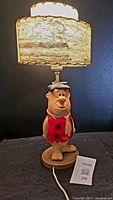 Front view of Fred Flintstone lamp with shade turned on showing the figurine base and textured shade.