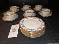 Six teacups and six saucers arranged with six small plates stacked separately, showing detailed gold trim and decorative patterning.