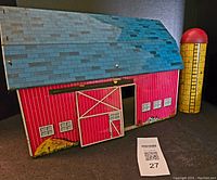 Image showing front and side of red lithographed tin barn with blue roof and attached yellow silo with red dome